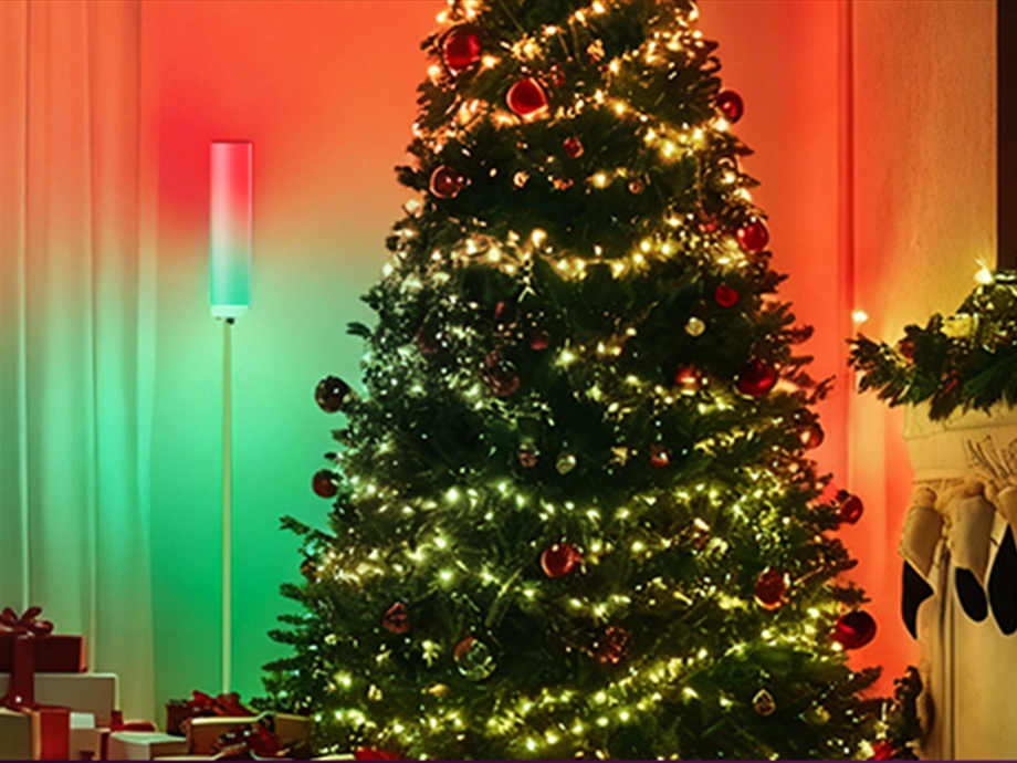 A Christmas tree decorated with lights, standing in a room next to a vertical lamp glowing orange and green.