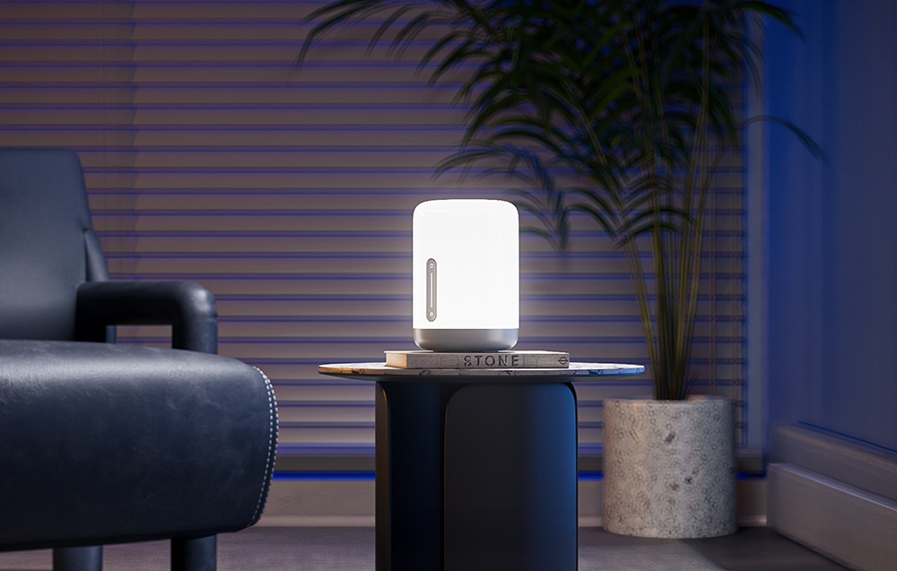 A lamp emitting a bright light on a side table in a modern living room with a potted plant in the background