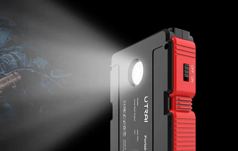 The built-in flashlight on the jump starter’s housing is illuminated, shining on the car’s engine.