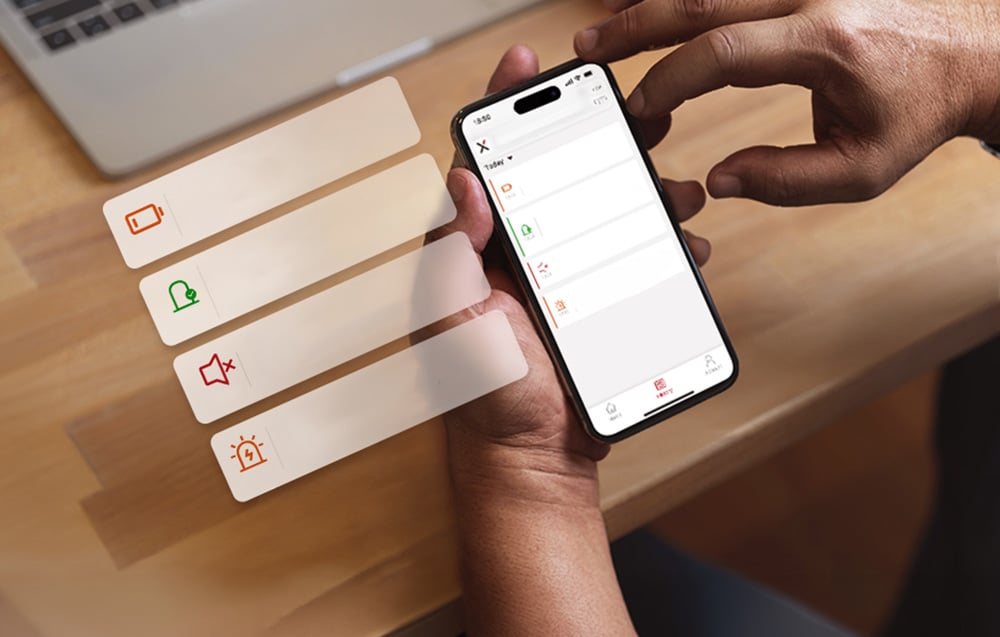 A hand holding a smartphone with an app displaying notifications about battery status and sensor alarms