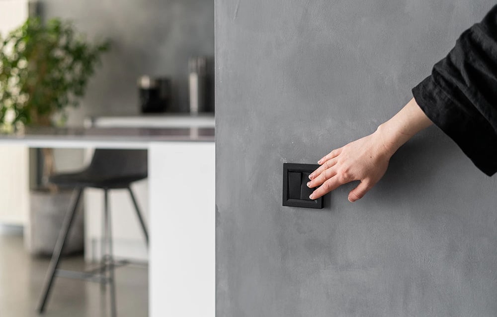 A hand pressing a black wall switch mounted in a gray concrete wall in a modern interior
