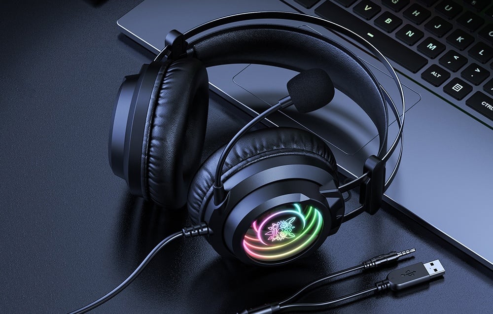 RGB backlit headphones lying next to a laptop with USB and jack cables on a dark desk