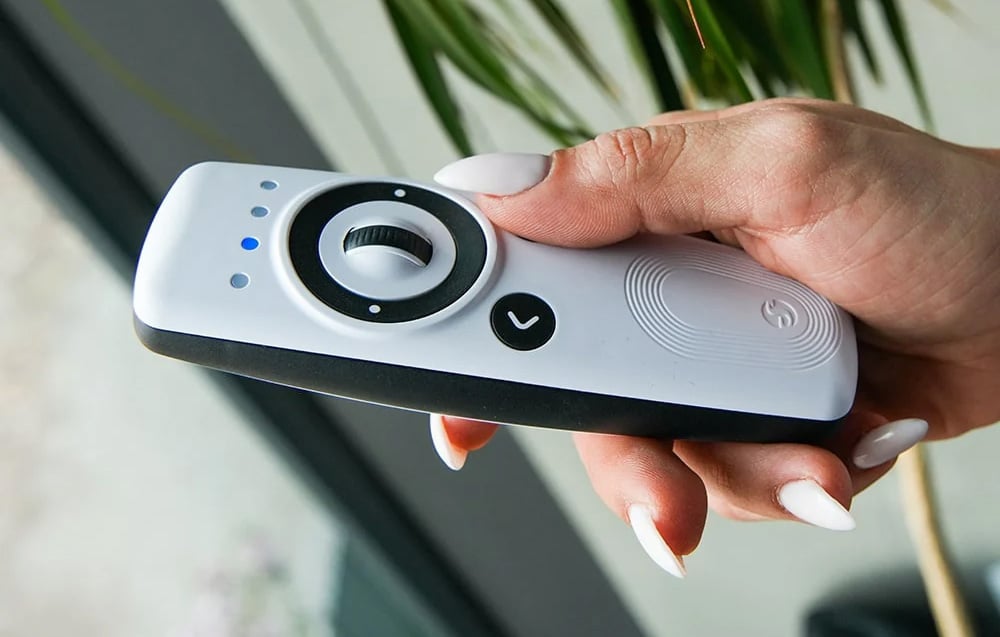 White Shelly remote control with dial and illuminated LED light held in right hand.