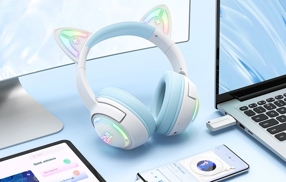 White headphones with blue accents lying on a desk next to a smartphone, tablet, laptop and monitor