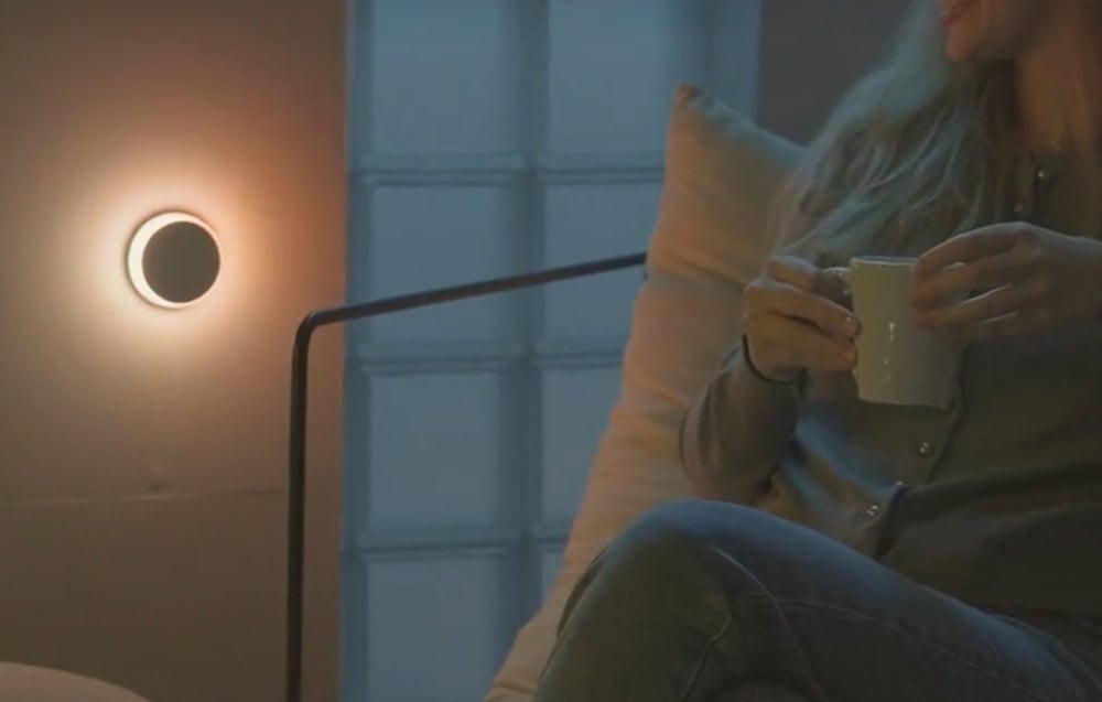 Yeelight Vega night light shining warm light on the wall next to a seated person holding a cup.