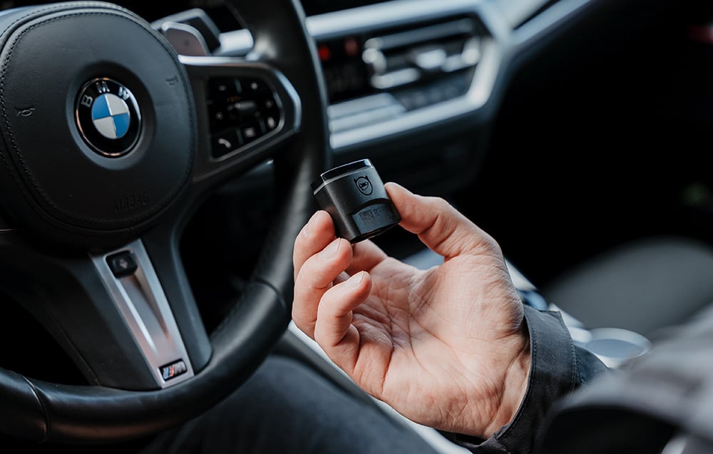 A hand holding Carly's OBD2 adapter inside a BMW car with the steering wheel visible in the background