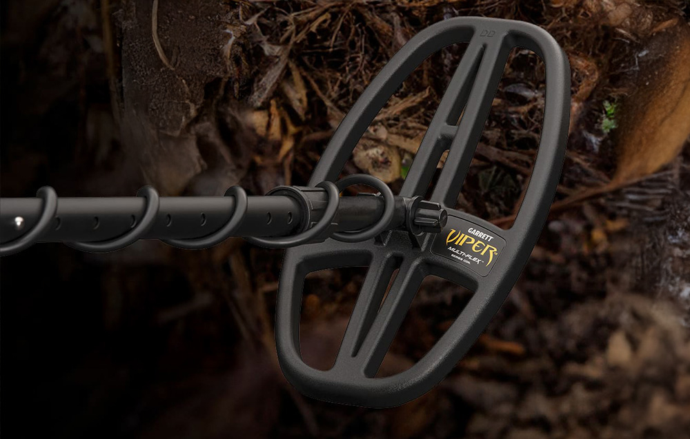Close-up of the metal detector's coil against a background of soil and leaves.