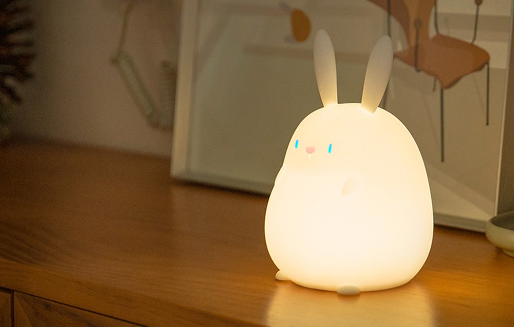 SuperFire RAB-02 Little Rabbit bedside lamp standing on a wooden shelf, emanating warm light.