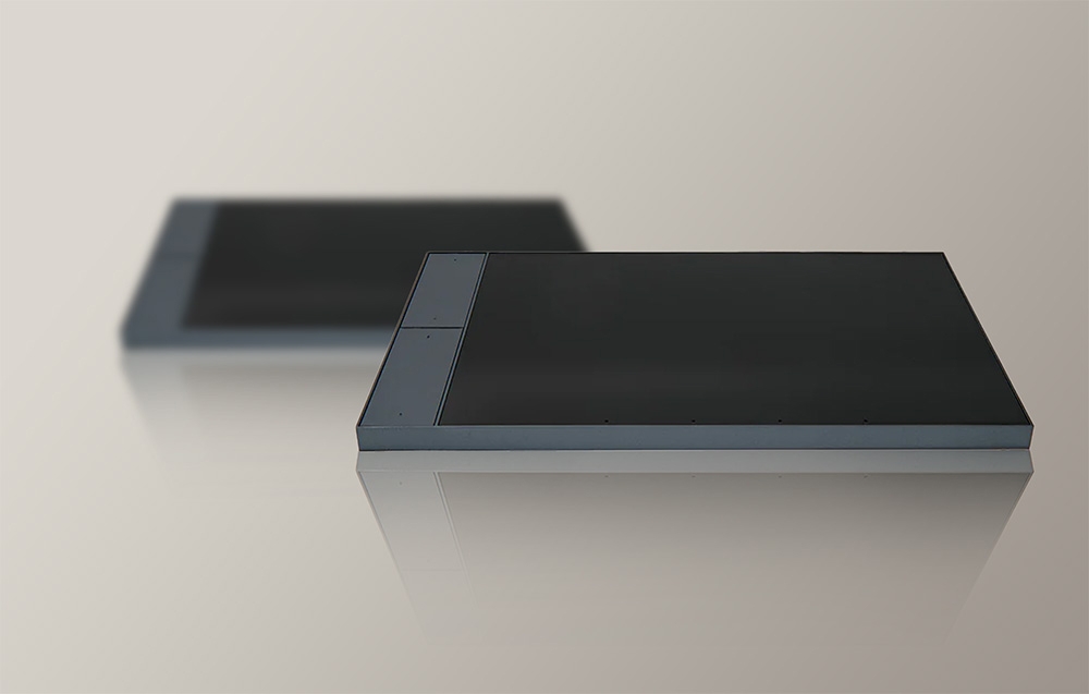 Two dark grey control panels with screens off lying on a beige surface