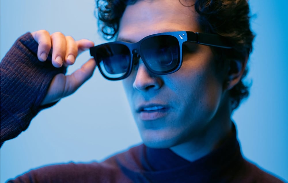 Man putting on black sunglasses against a background of blue light