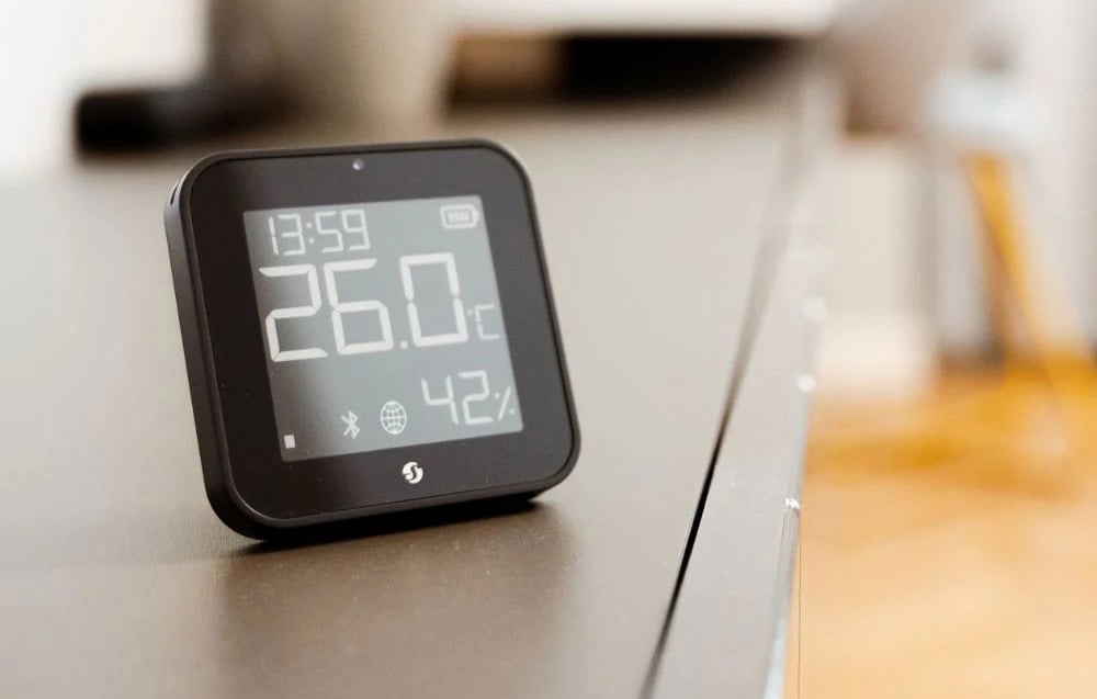 A modern black temperature and humidity sensor placed on a smooth piece of furniture