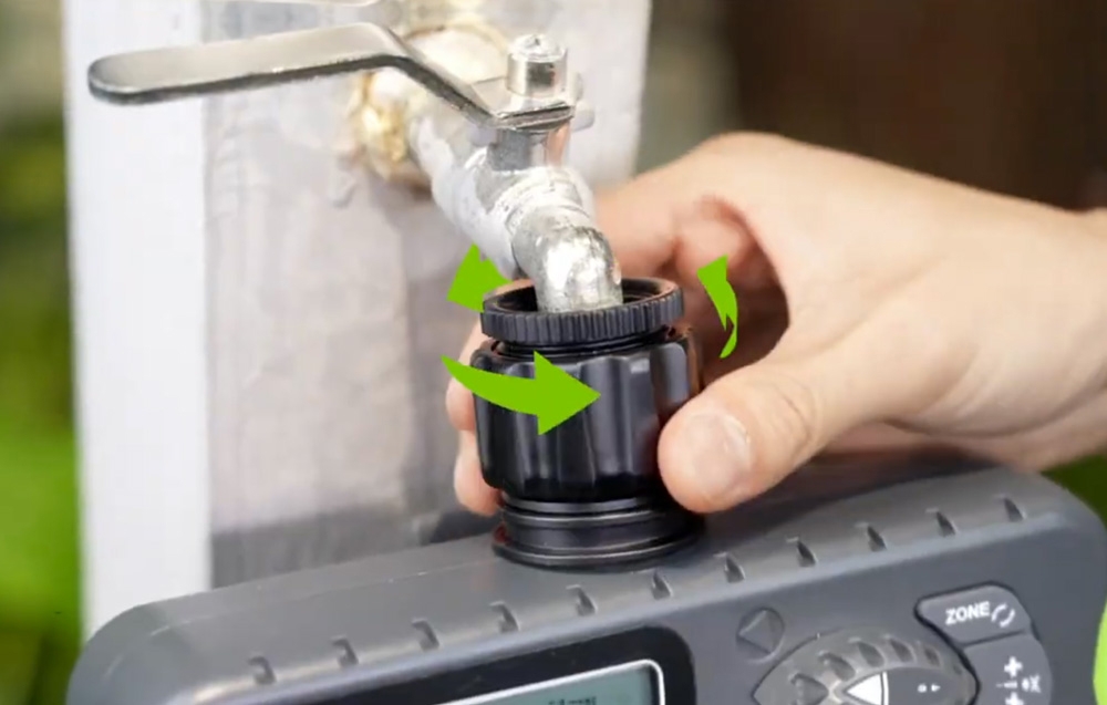 A hand turning the RainPoint 4-zone irrigation controller off the outdoor faucet