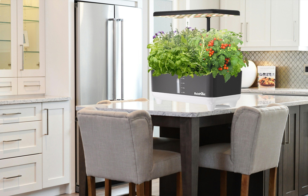 A hydroponic garden with herbs and tomatoes sits on a marble dining table in a modern kitchen