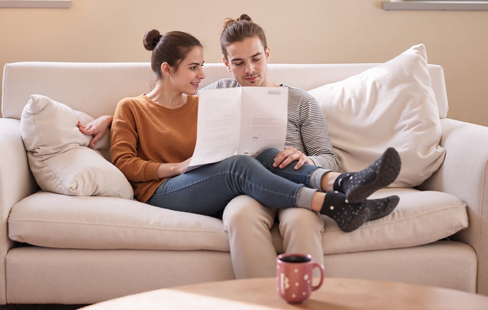 A couple sitting on a light-colored sofa in the living room, reviewing documents