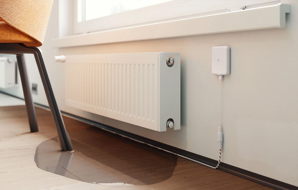 Flood sensor near the radiator in the room with a puddle of water on the wooden floor