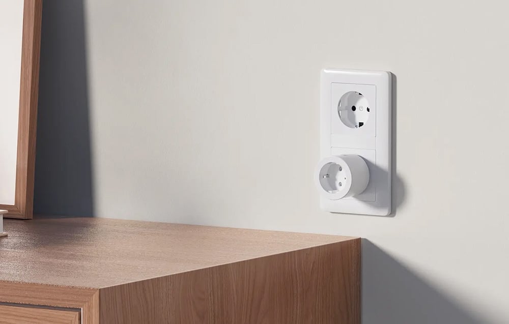 A white smart plug plugged into a vertical wall outlet above a wooden cabinet