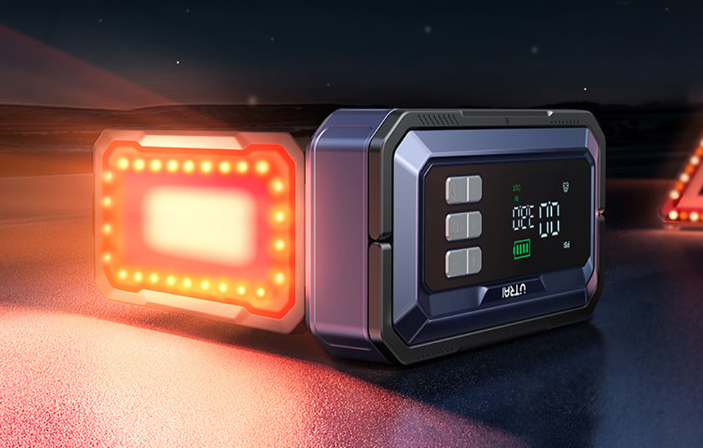 A car jump starter lying on the road with a red warning light illuminated.
