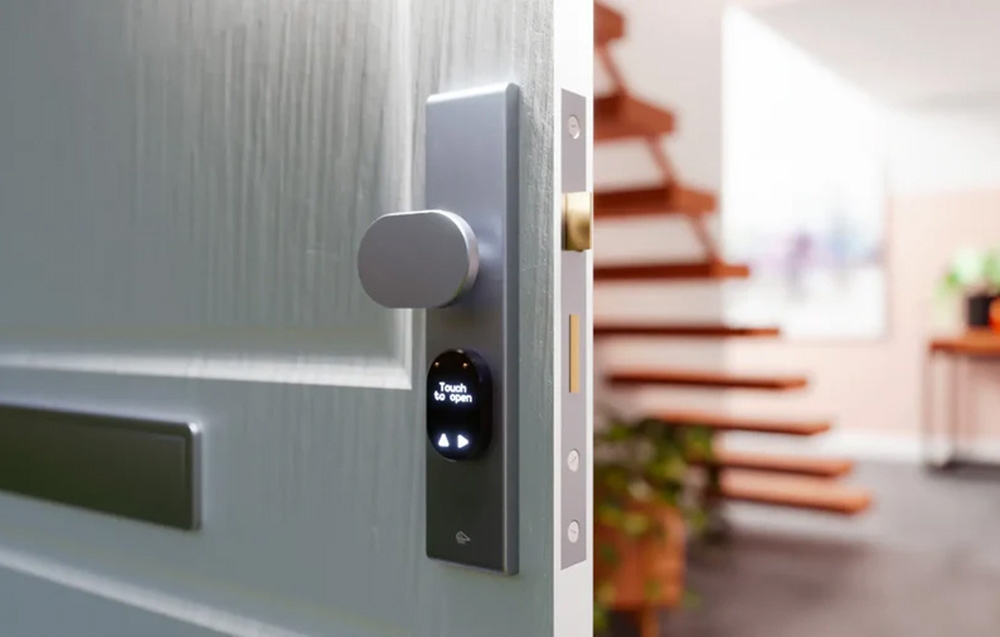 A silver doorknob on a white door with a small, oblong display that reads “Touch to open”