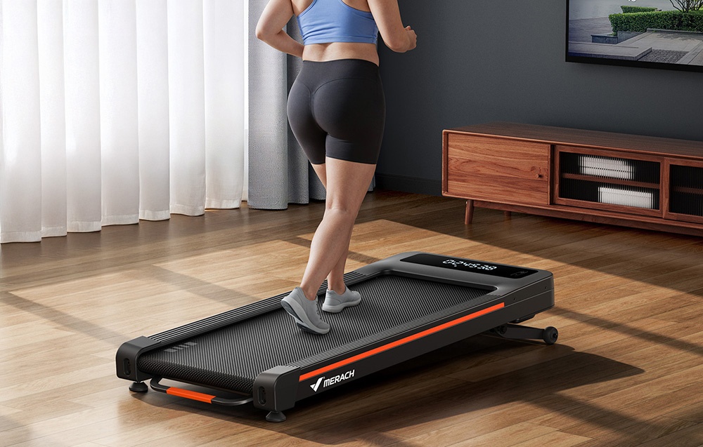 A woman seen from behind while walking on a black Merach treadmill with an orange belt in a room