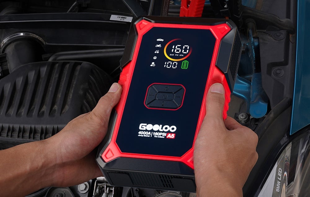 A man’s hands holding a red-and-black Gooloo jump starter over an open car hood