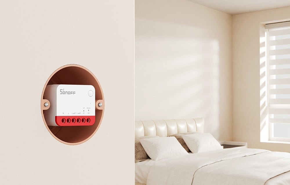 SONOFF control module placed in a round housing on the wall of a bedroom with a white bed and window blinds.