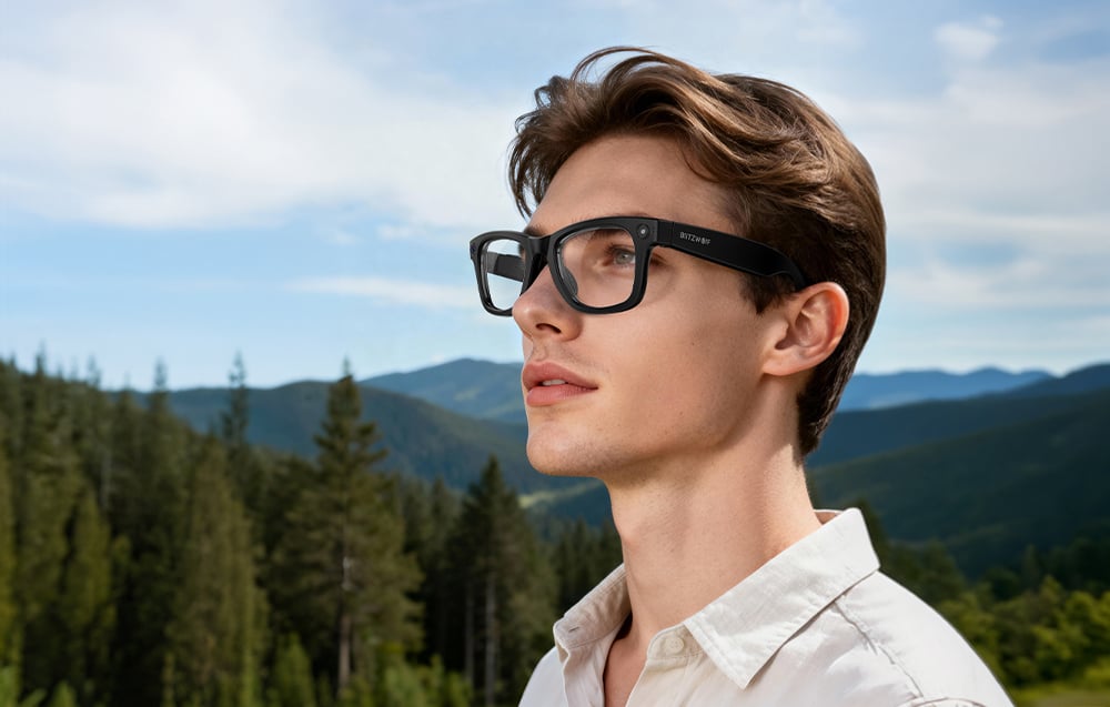 A man wearing glasses and a white shirt against a backdrop of mountains and trees