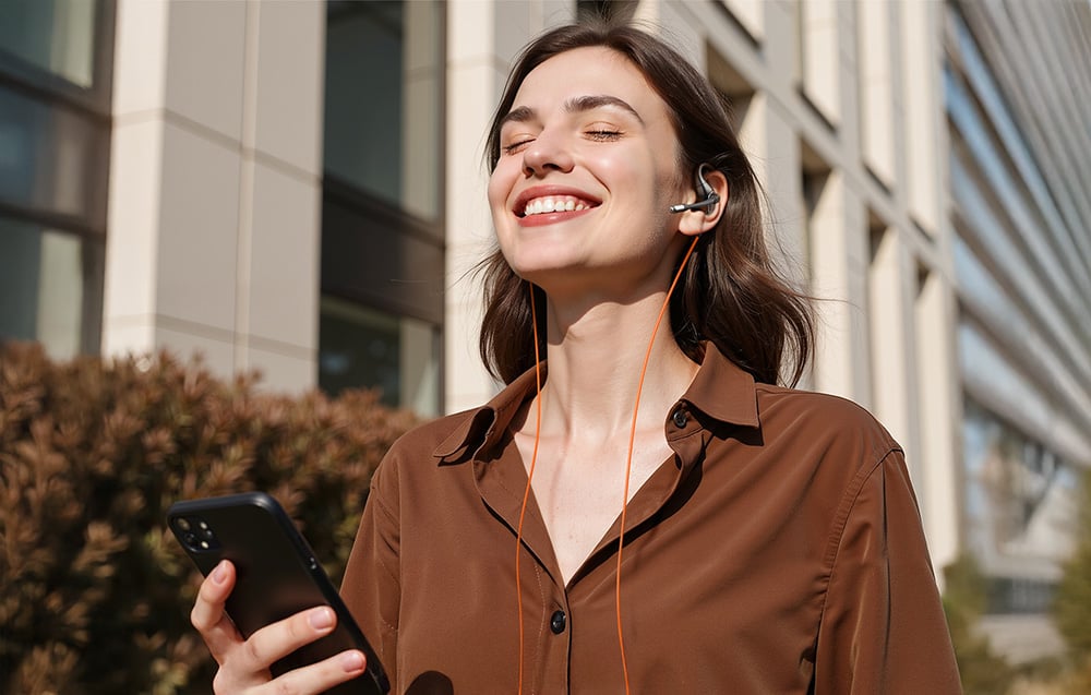 Woman outside holding phone and smiling, wearing headphones with microphone