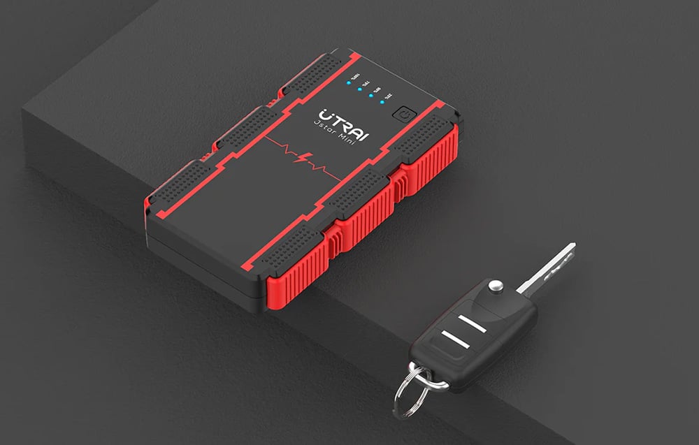 A handy black-and-red jump starter lying on a dark countertop next to a car key.