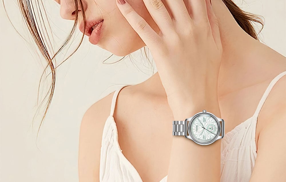 Close-up of a woman's wrist wearing a silver COLMI smartwatch on an elegant bracelet, matching her white dress.