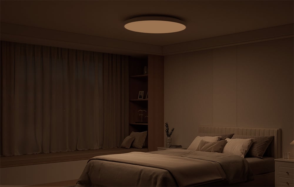 A darkened bedroom interior with a bed and the Yeelight Mercury C300 ceiling lamp glowing in warm light.