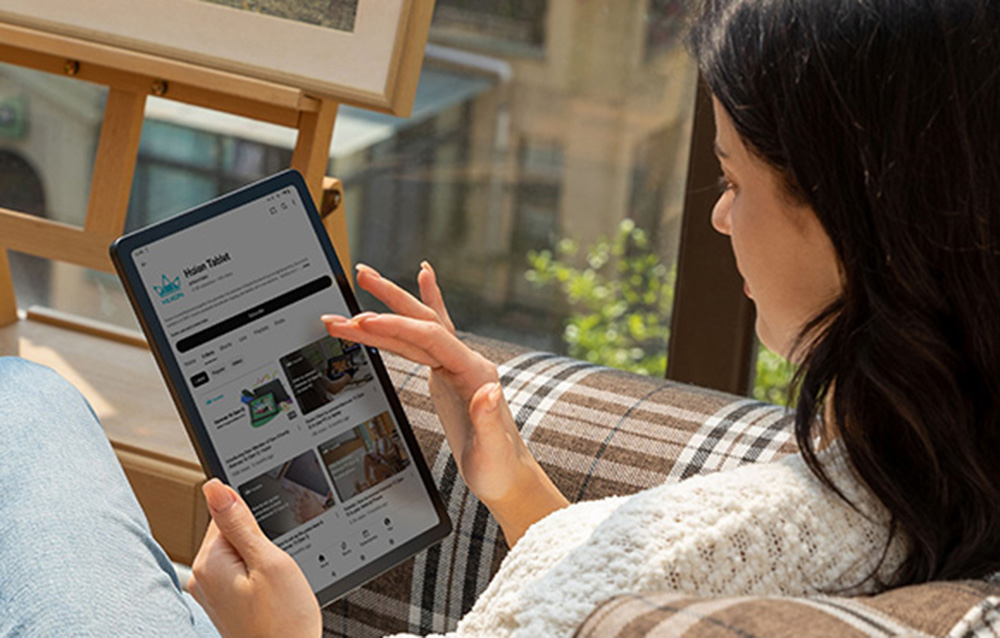 Woman browsing Huion Tablet website on tablet, sitting comfortably by the window