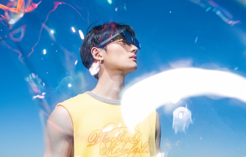 A man wearing glasses and a yellow T-shirt looks up against the backdrop of a blue sky with glints of light