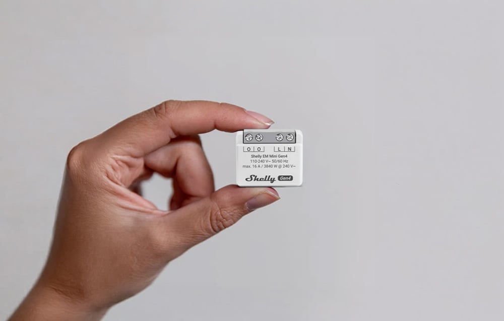 A person holding a white energy meter with visible screw terminals between two fingers.