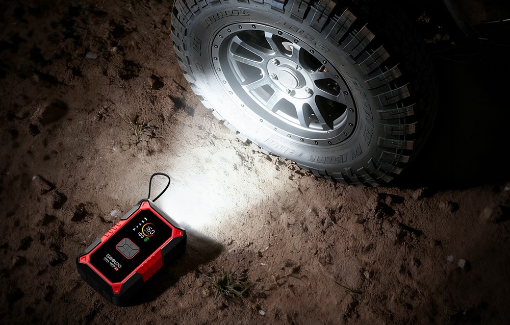 The jump starter illuminating a wheel of an off-road vehicle on sandy ground at night
