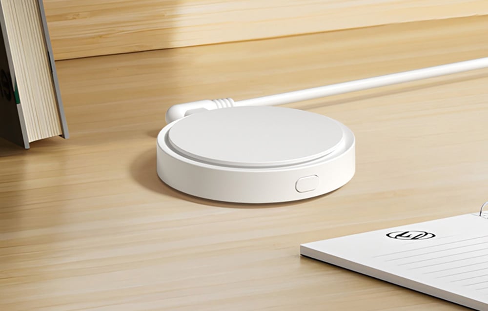 White sensor with wire lying on a wooden countertop next to a book and notepad