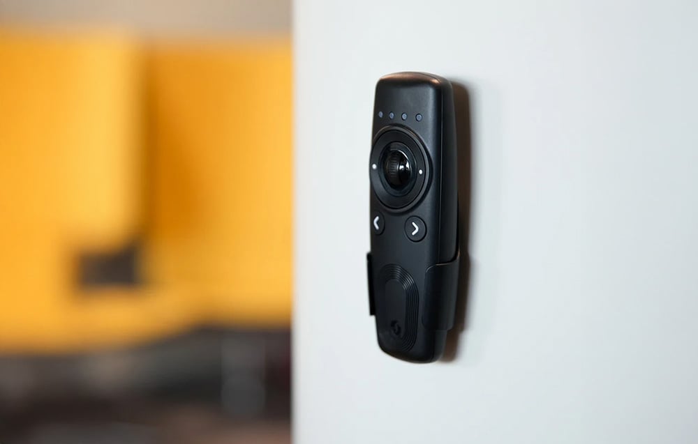 Shelly BLU remote control mounted on a wall in a holder, with visible arrow buttons and a central knob