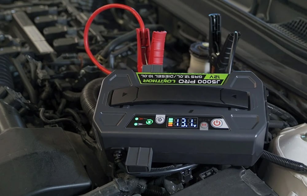 The jump starter placed on the car’s engine, with a visible display showing the current voltage.