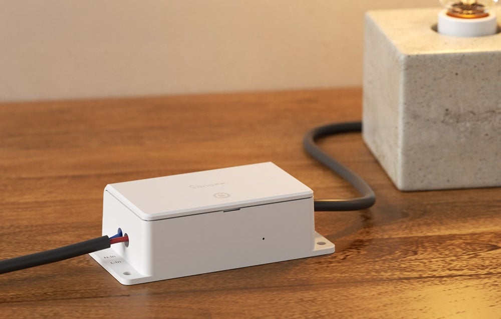 White Sonoff smart relay with connected cables on wooden surface