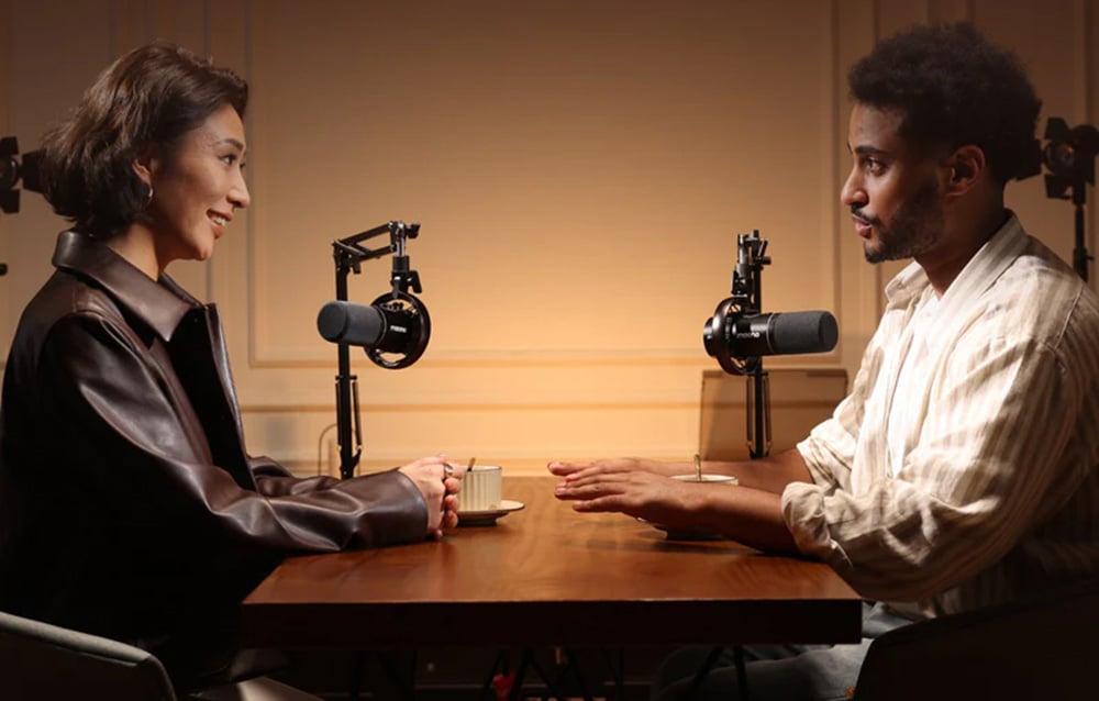 A woman and a man sit at a table and talk, there are microphones next to them