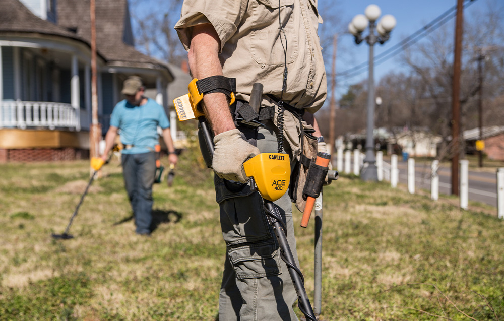 A person with a metal detector searches the lawn in front of a house.