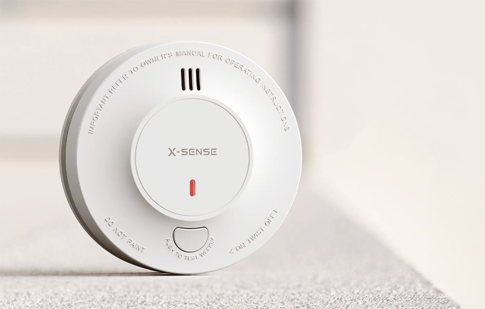 Close-up of the X-Sense smoke detector with a red LED on a light background