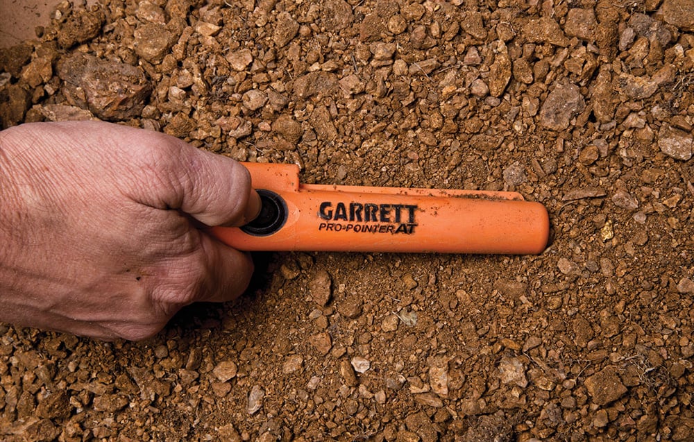 A person holds the metal detector above the ground full of rocks.