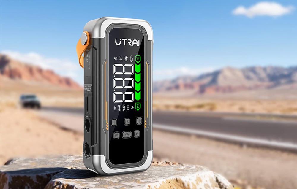 A car starter with its screen turned on sits on a rock by an asphalt road.