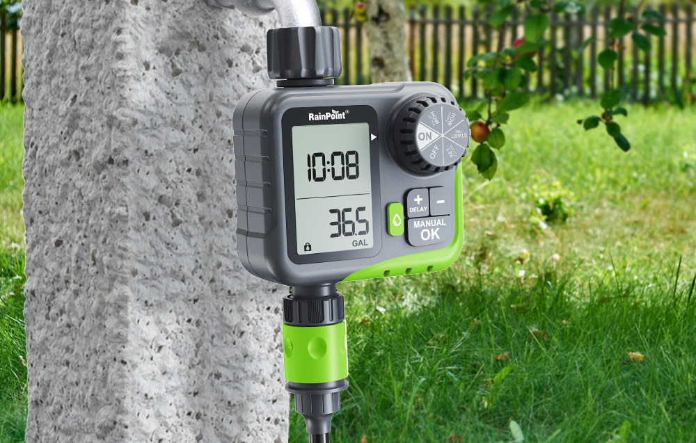 RainPoint controller mounted on a faucet next to a concrete post against the backdrop of a green lawn and orchard