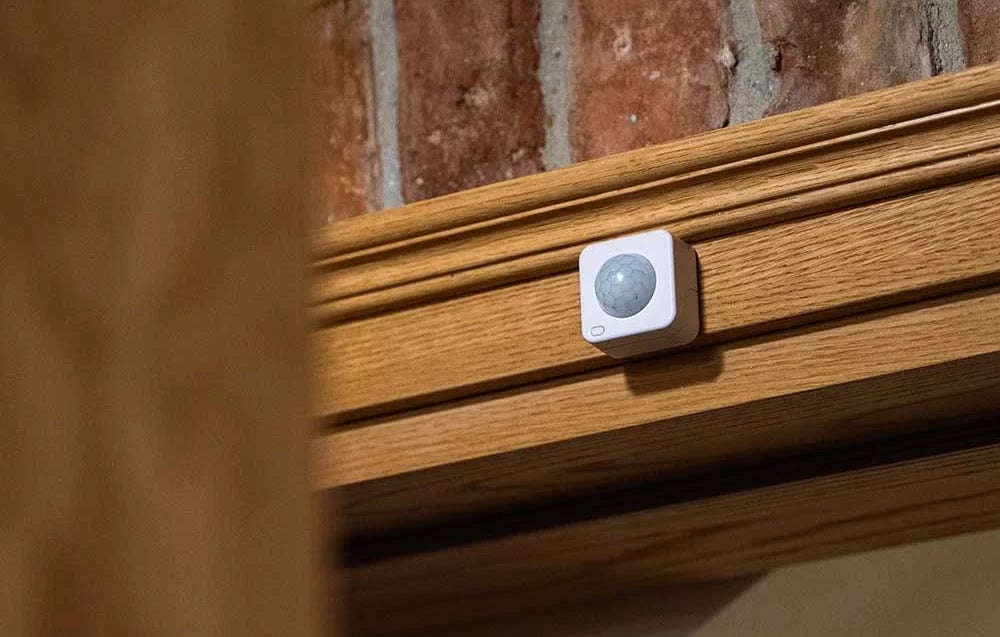 A white, square device with a round, gray lens mounted on a wooden door frame