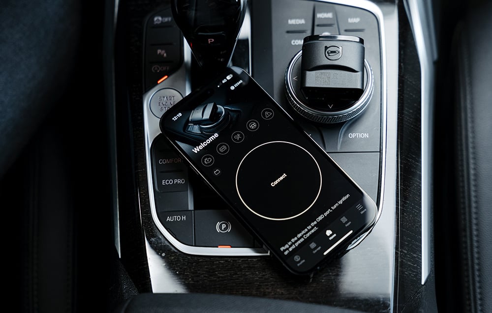 Black Carly remote control connected to OBD2 port on BMW car, displaying welcome screen