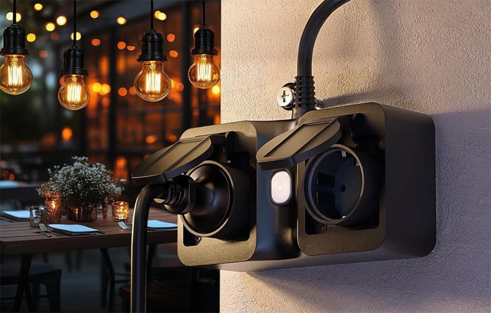 Double outdoor outlet with one connected cable, mounted on the wall near the illuminated terrace