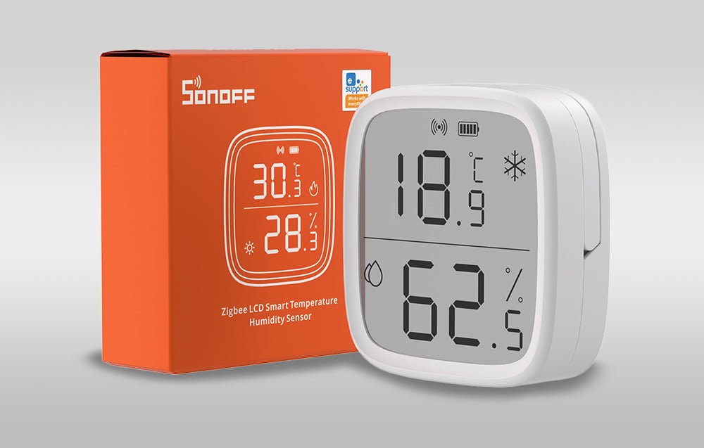 A temperature and humidity sensor next to an orange package on a light background