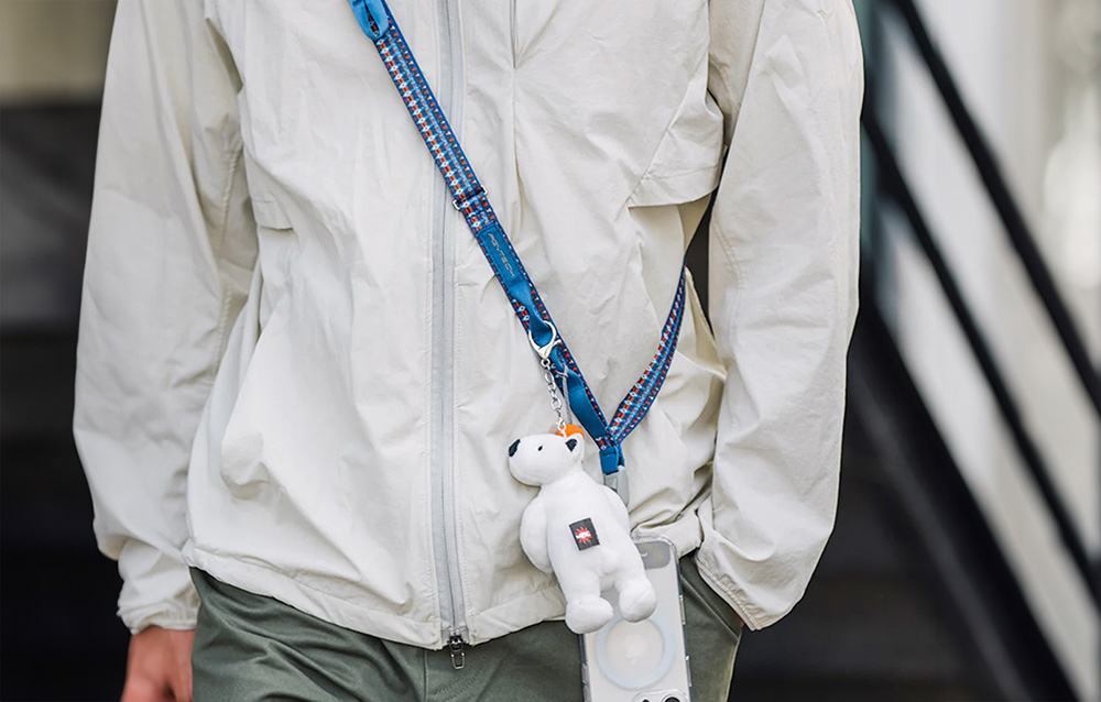A person in a white jacket wears a PGYTECH strap around his neck, to which a smartphone and accessories are mounted