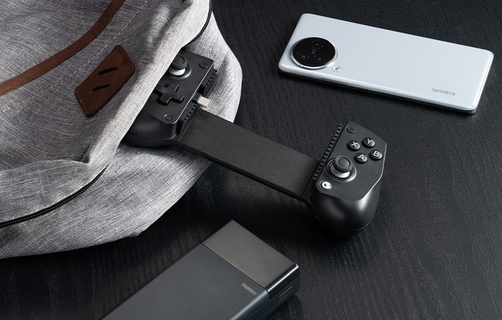 Black GameSir controller partially protruding from backpack, next to smartphone and powerbank on black table.